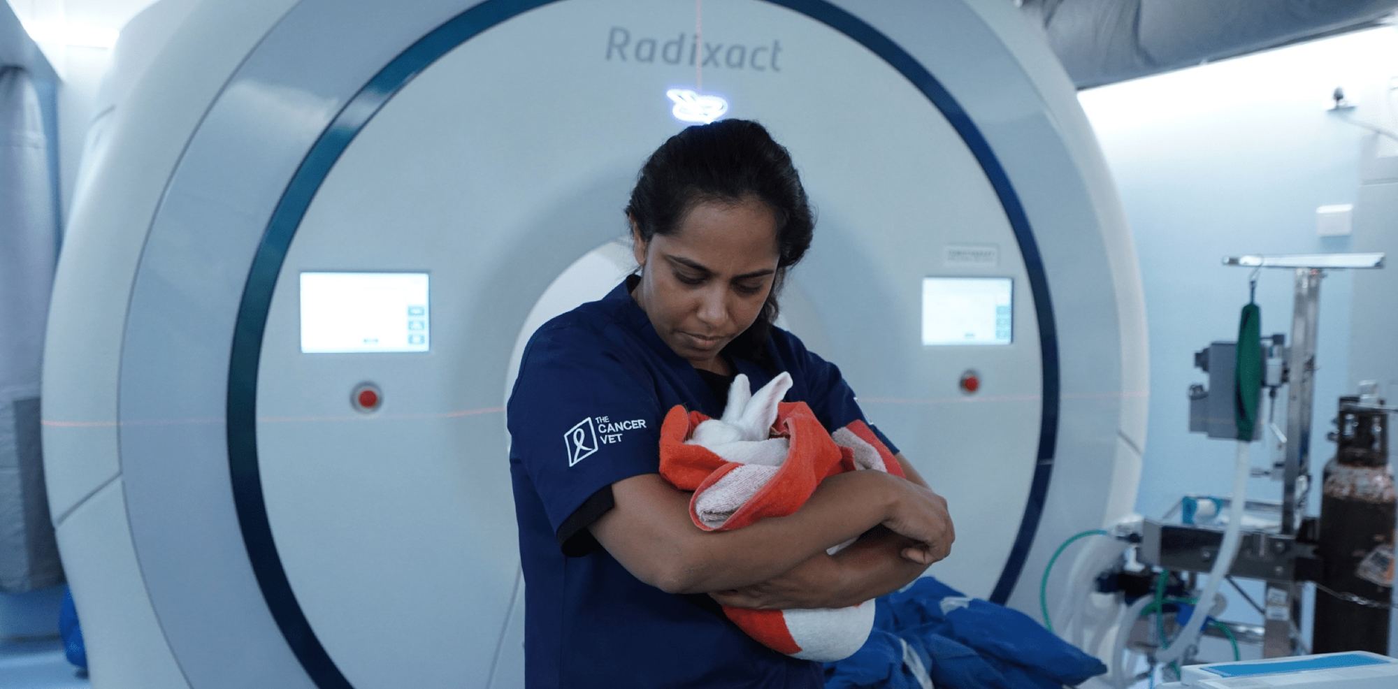 A clinician in navy scrubs holds a small wrapped animal in front of a large ring-shaped Accuray Radixact radiotherapy machine