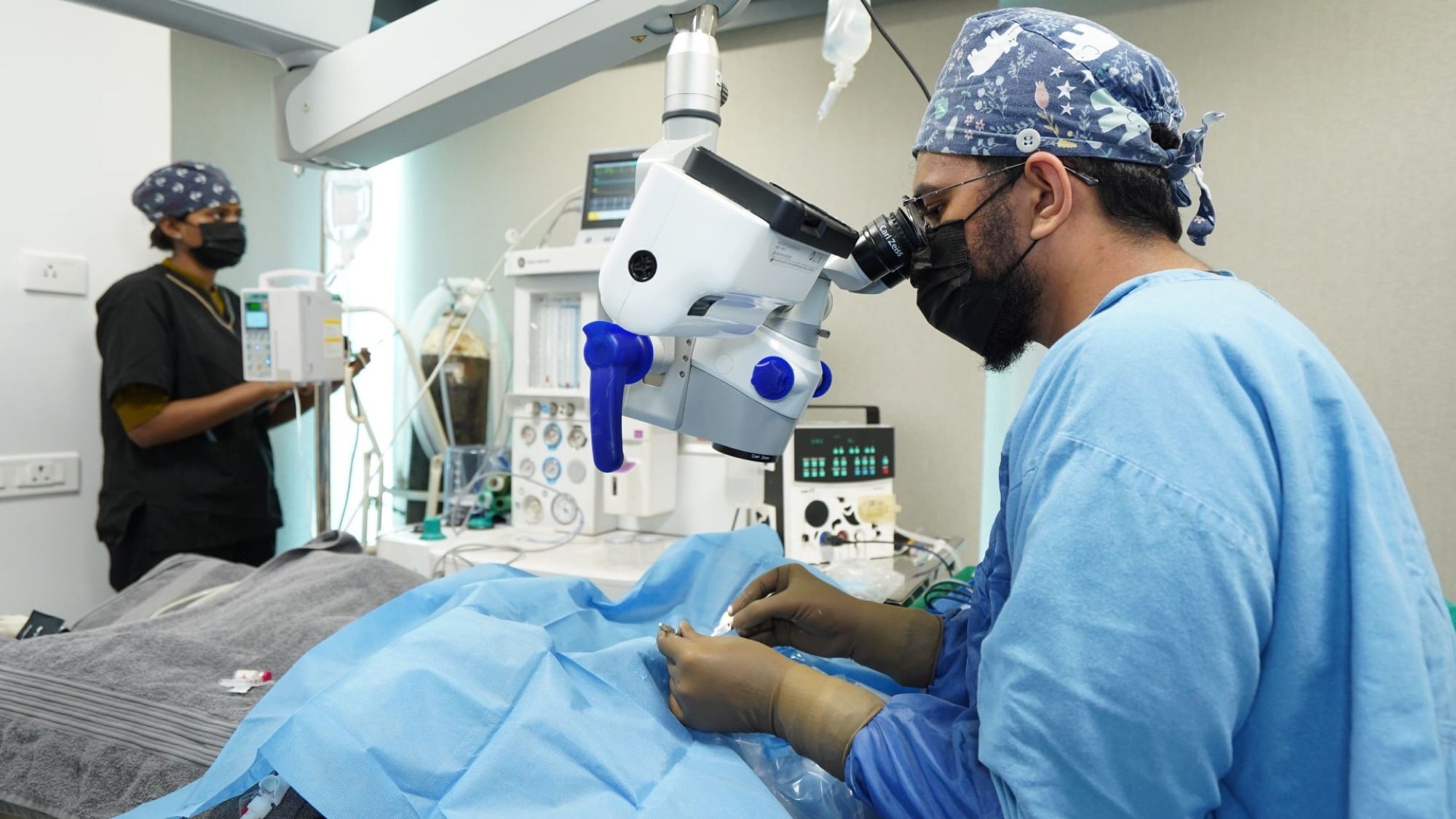 Two gowned surgeons working at an ophthalmic operating microscope, one passing an instrument