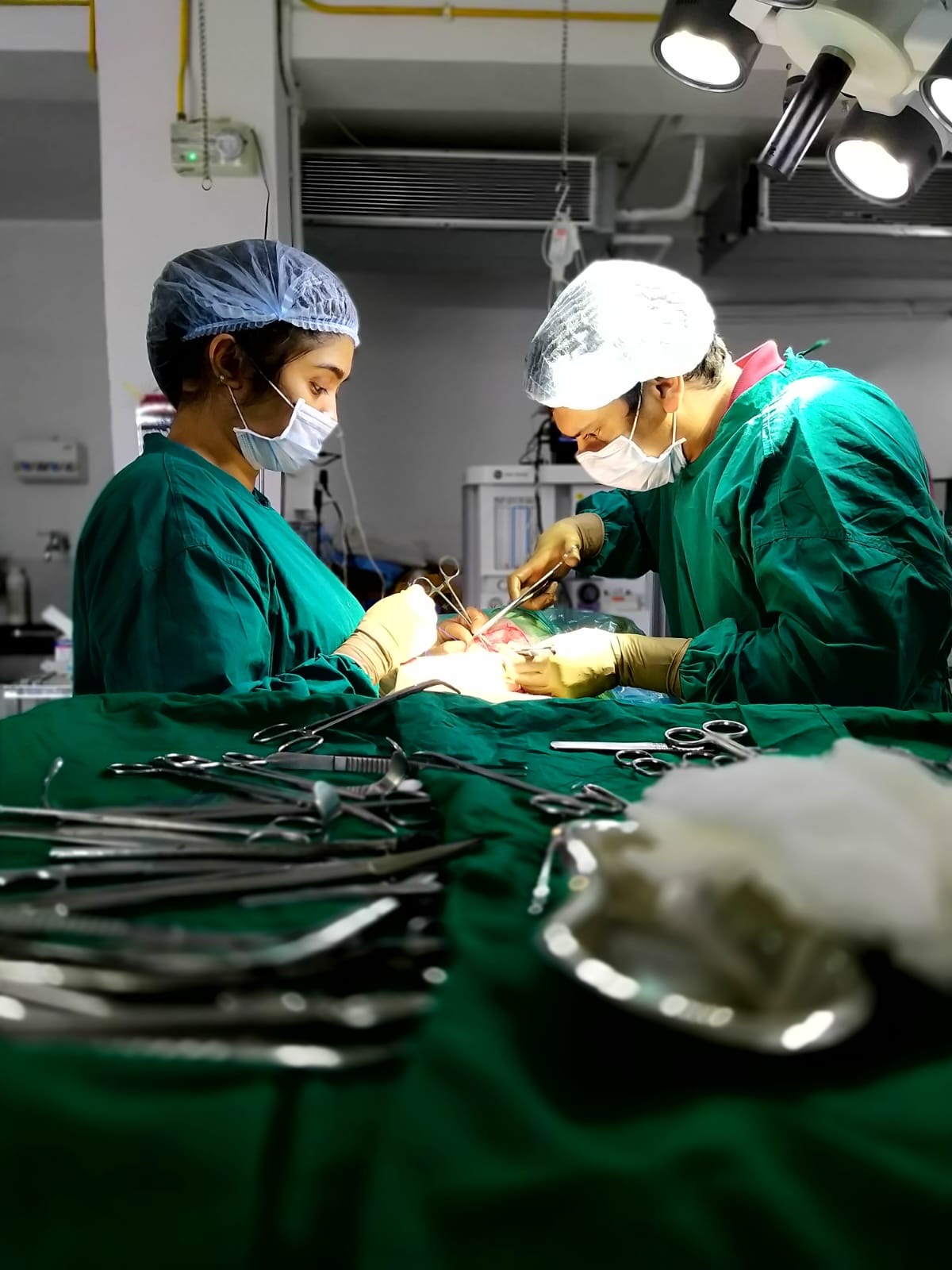 Two surgeons in full scrub operating on a draped patient with instruments laid out